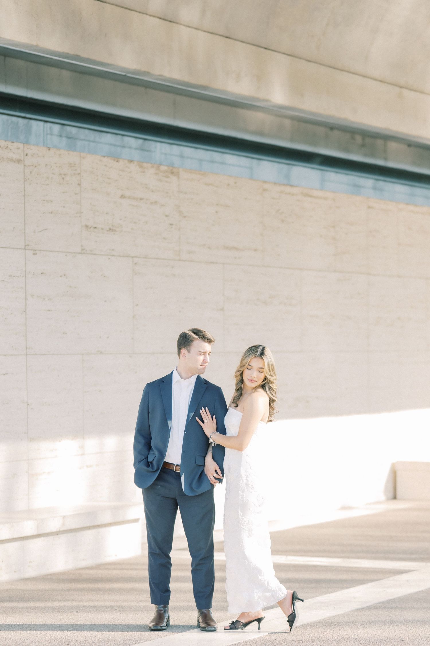 A couple in formal attire poses playfully in a series of minimalist architectural photos against a light concrete wall.