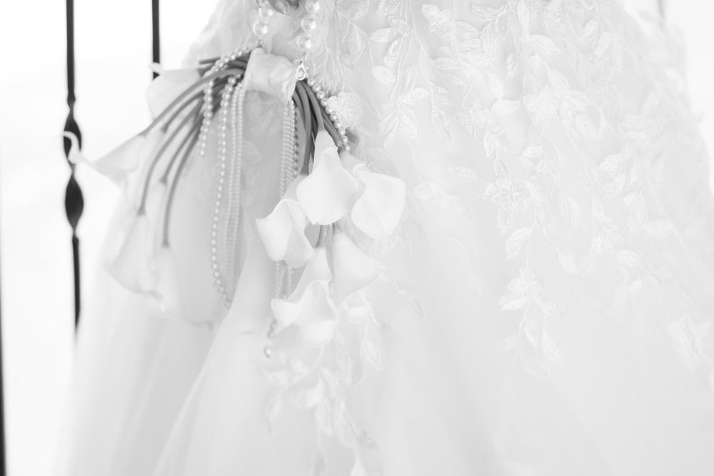 Close-up detail of white calla lilies and delicate lace on wedding dress.