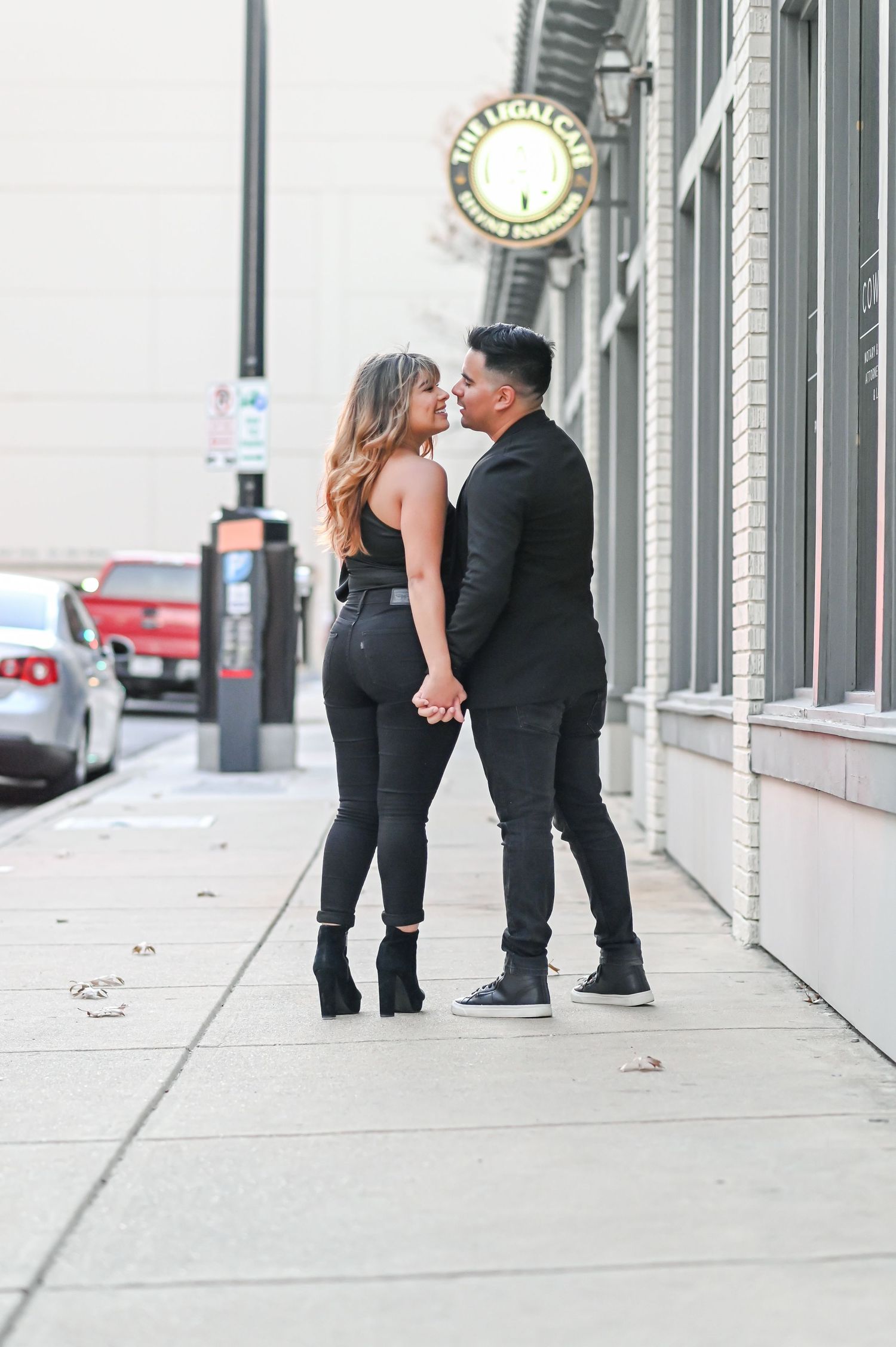 A romantic couple holds hands and shares a kiss on a downtown city sidewalk.