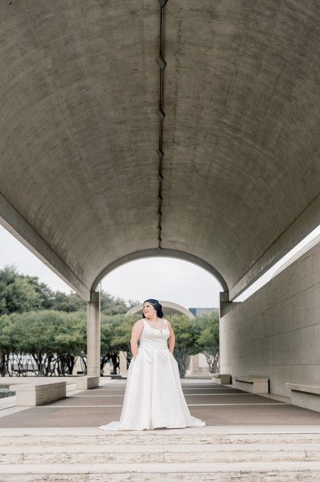 Bride in white ball gown standing under concrete arch tunnel during outdoor bridal portrait session.