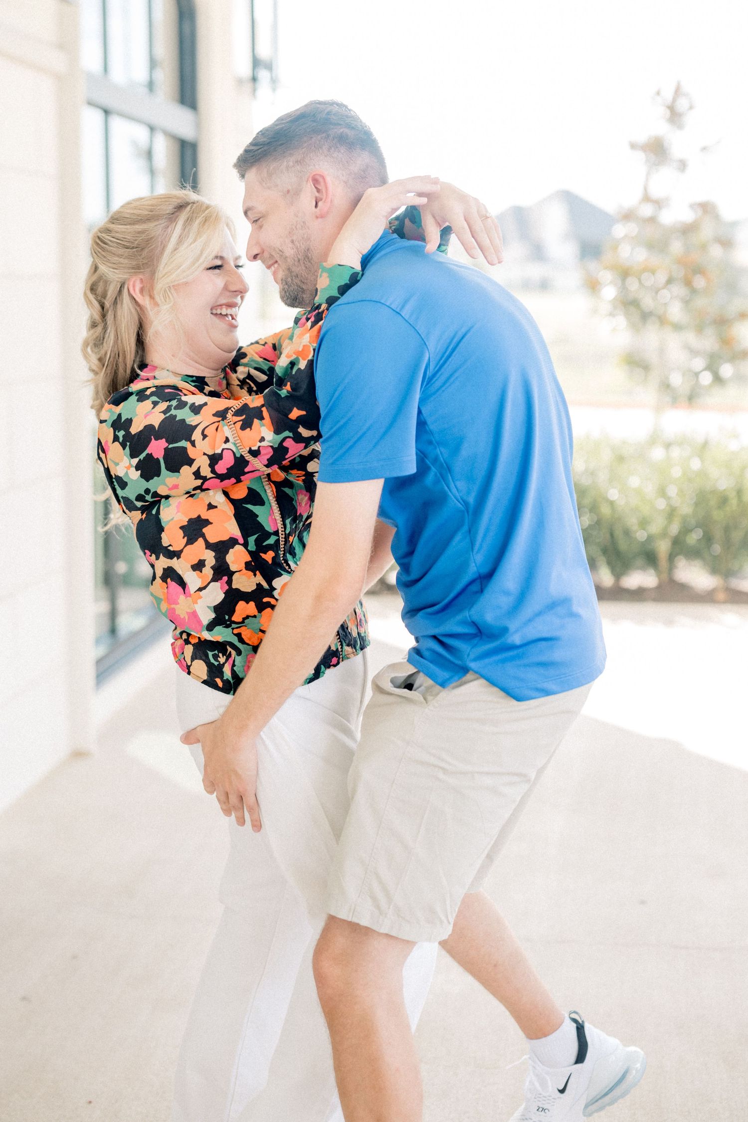 Laughing couple dancing outdoors, woman in floral blouse and man in blue polo sharing a joyful moment.