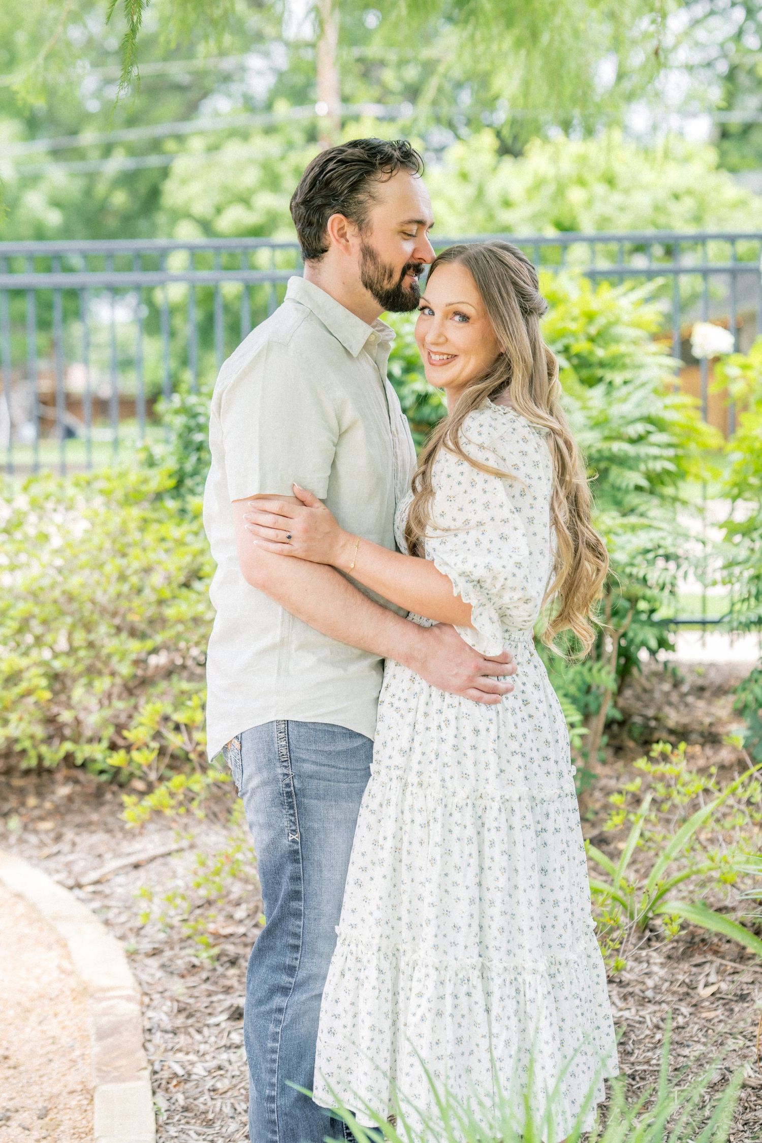 Couple sharing a tender embrace in a sunny garden with lush green foliage.