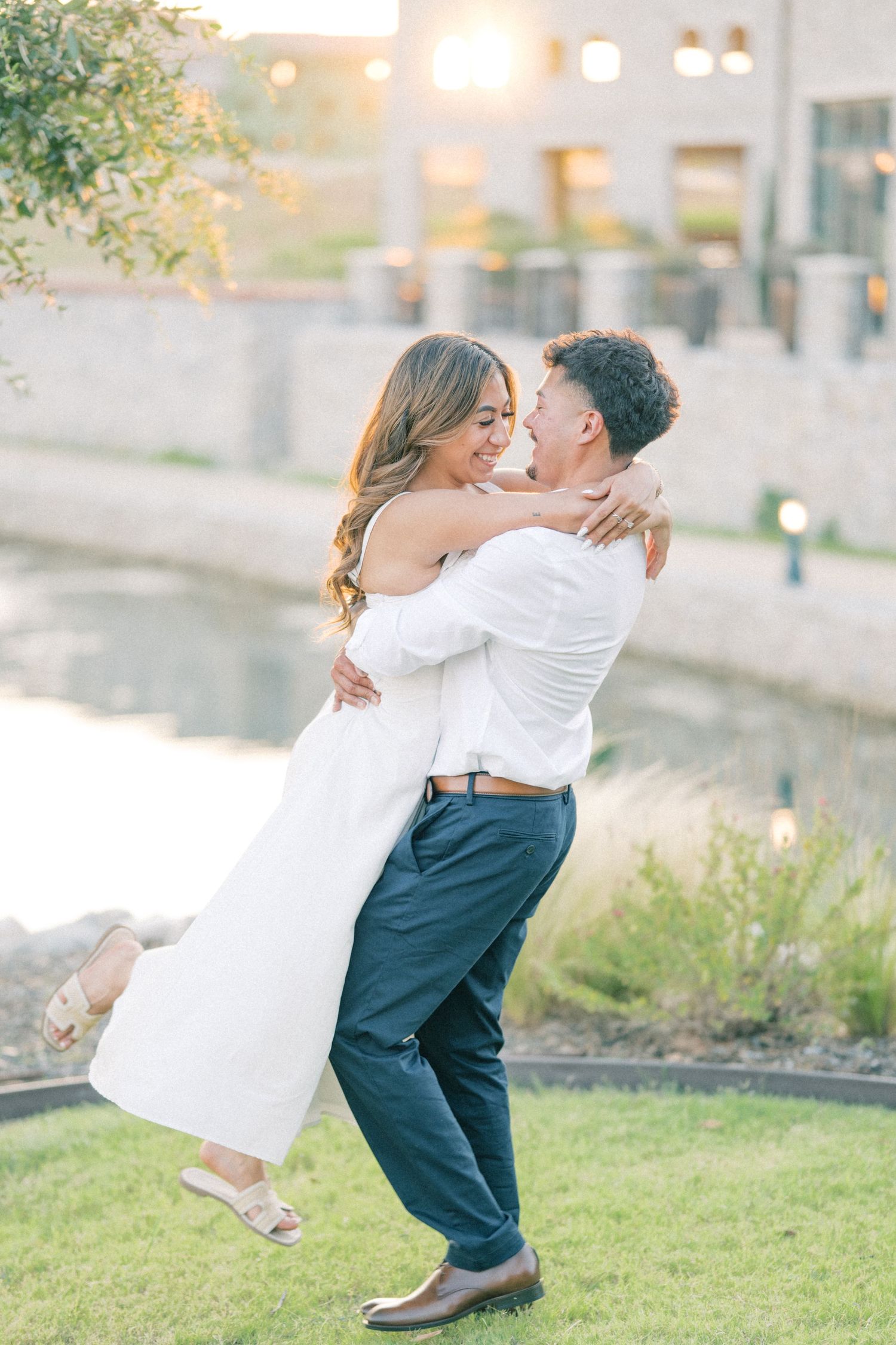 A joyful man lifts his partner in his arms as they smile at each other during their engagement shoot.