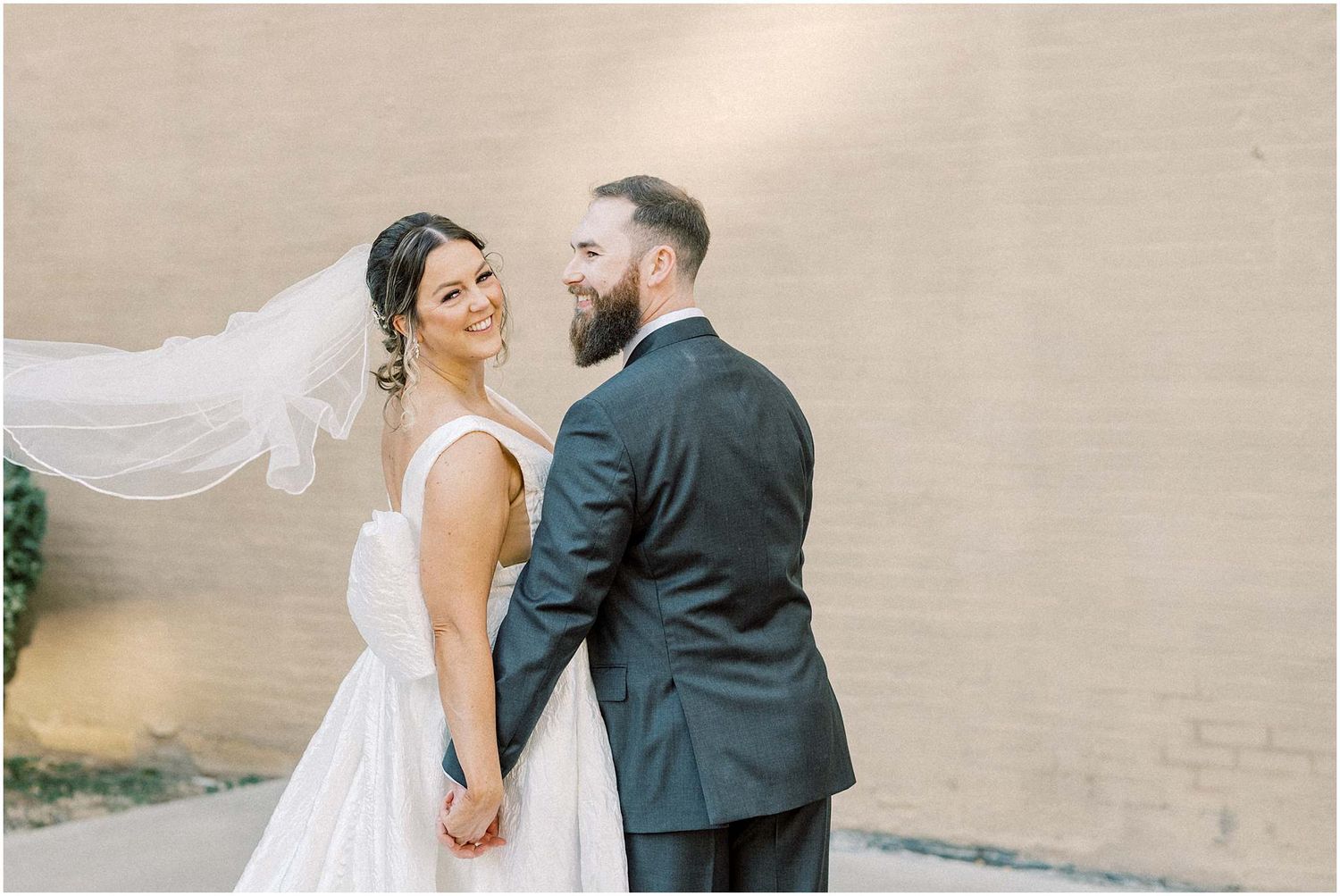 Romantic wedding portraits against a beige wall in natural lighting.