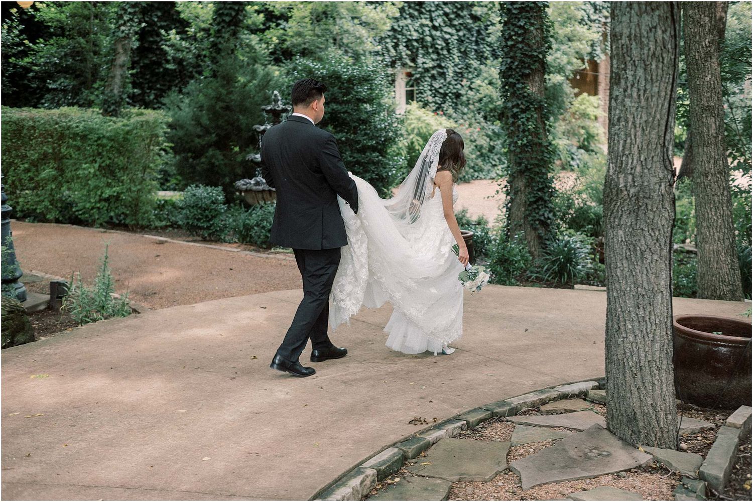 Couple shares romantic moments along a tree-lined garden path during their wedding photoshoot.