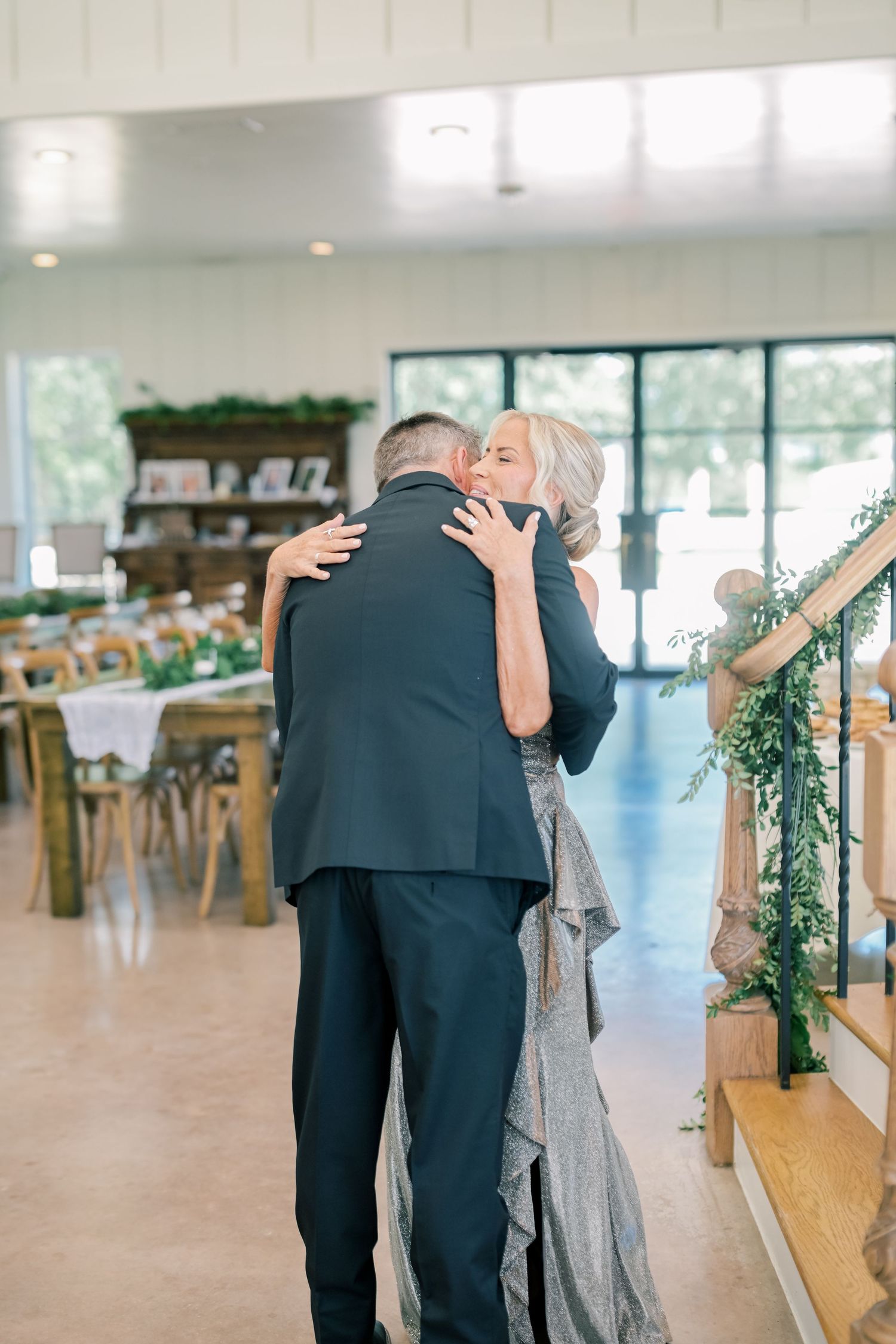 Mother and son share a warm embrace during an elegant wedding reception with greenery decor.