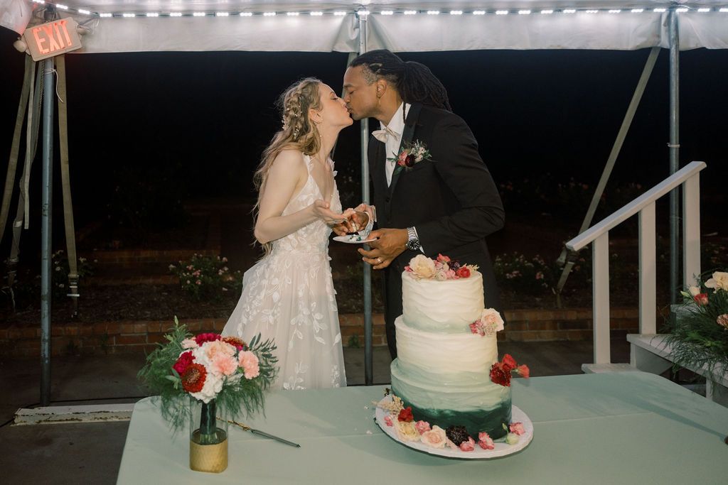 Bride and groom kiss while cutting their elegant three-tier wedding cake at their reception.