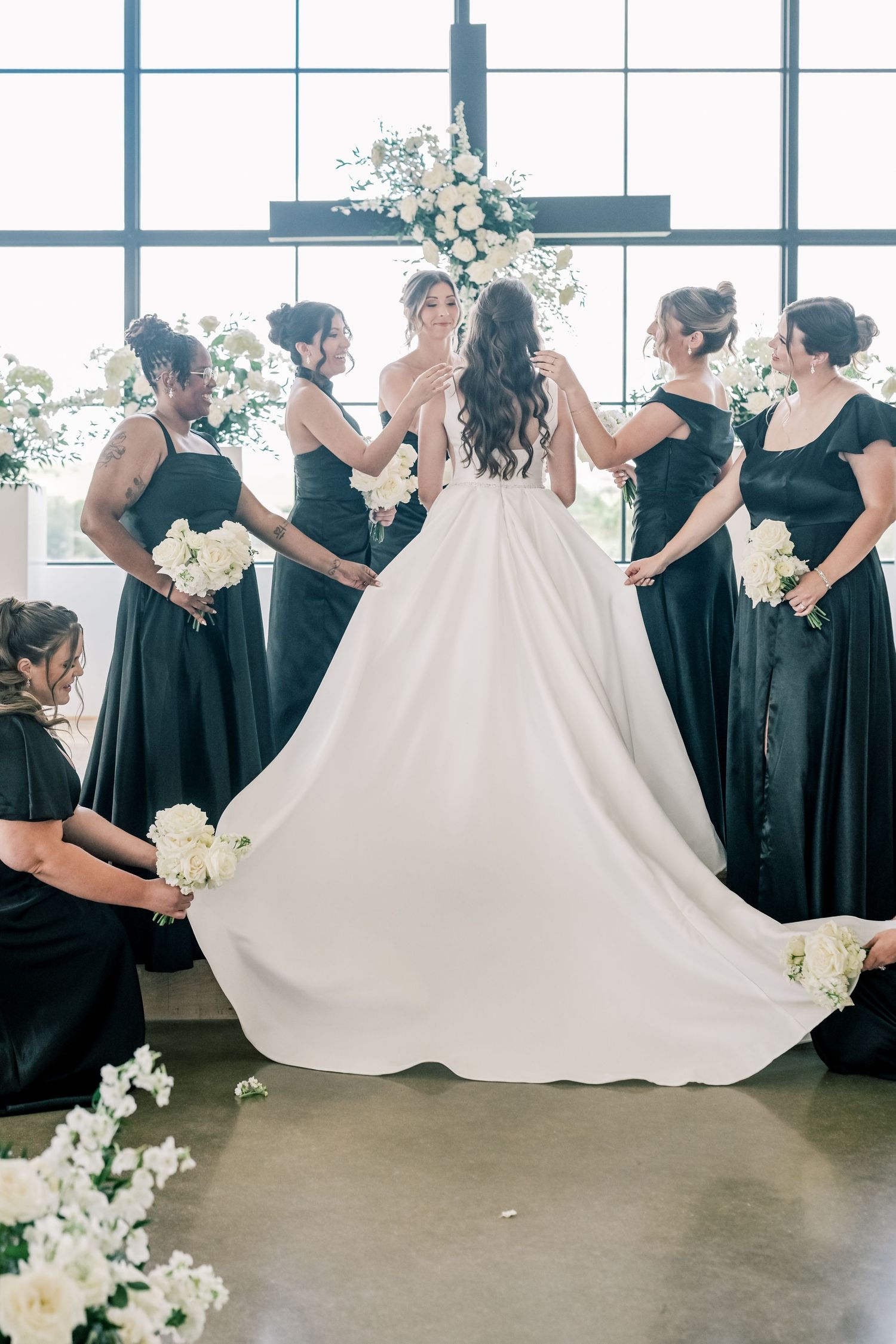 Bridesmaids in black gowns arrange the bride's white ballgown train at the altar.