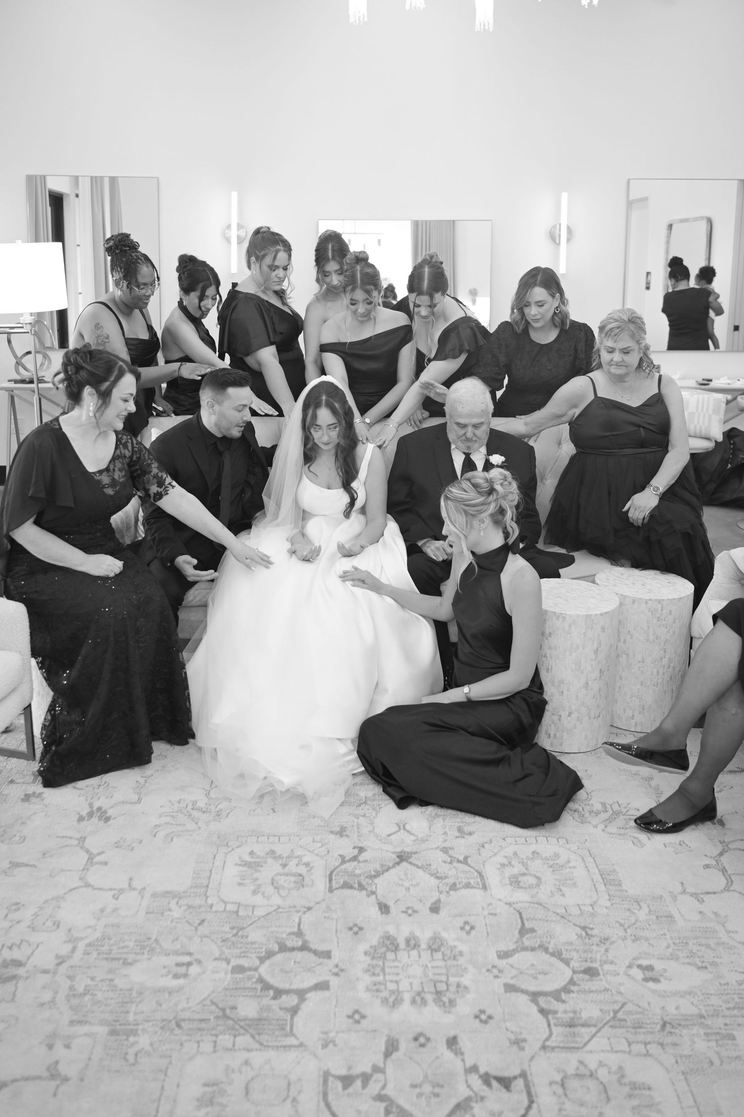 Black and white photo of bridesmaids and family praying over bride before wedding ceremony.