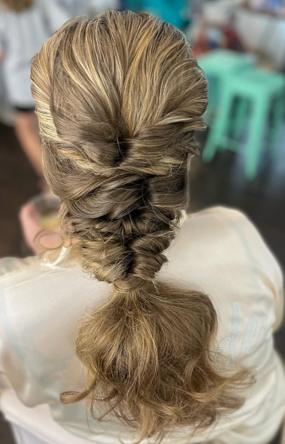 Close-up of an elegant braided low ponytail hairstyle with blonde highlights, styled in a loose fishtail braid.