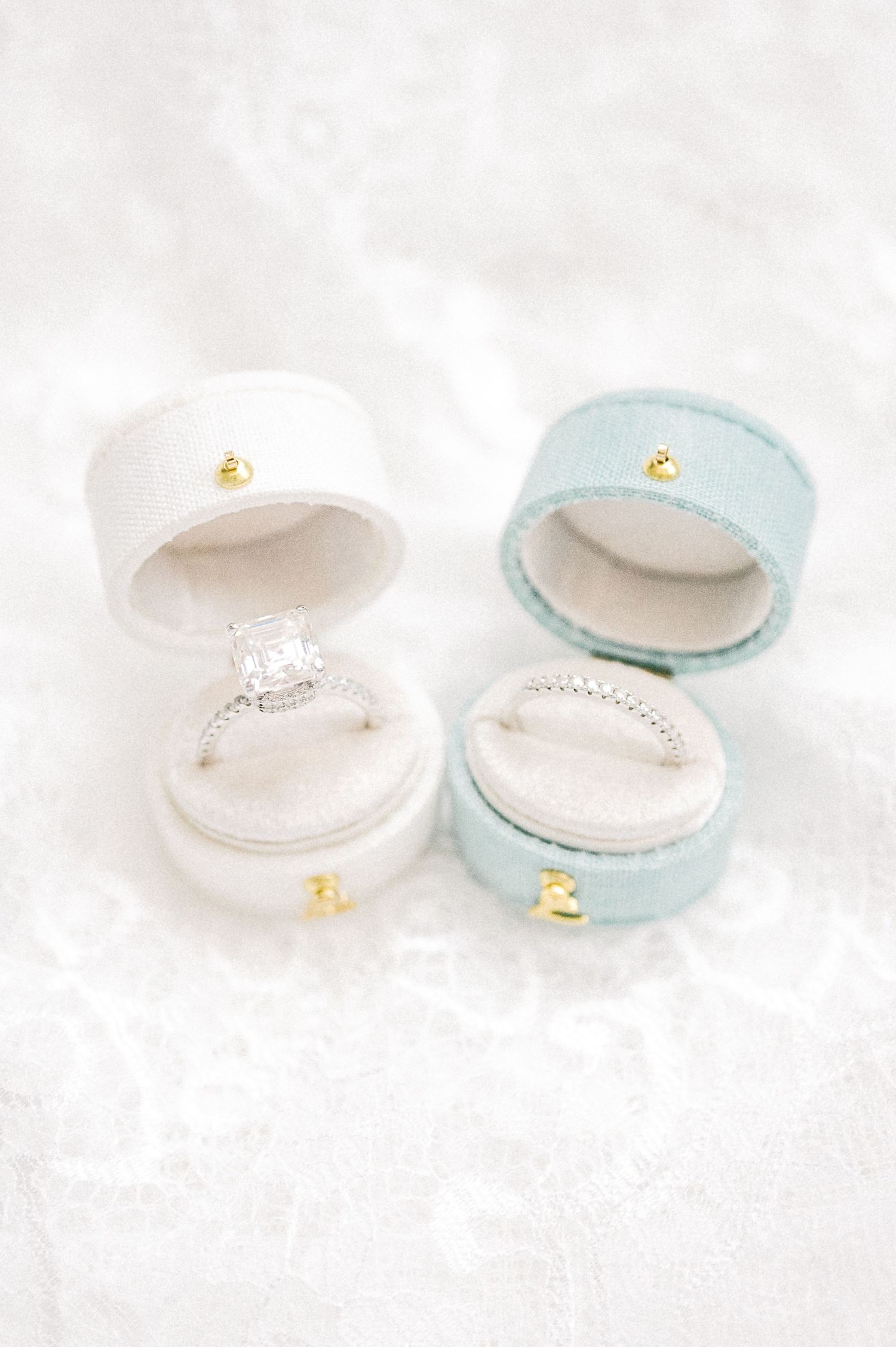 Two elegant rings displayed in open velvet ring boxes, one white with a diamond halo ring and one blue with a diamond band.