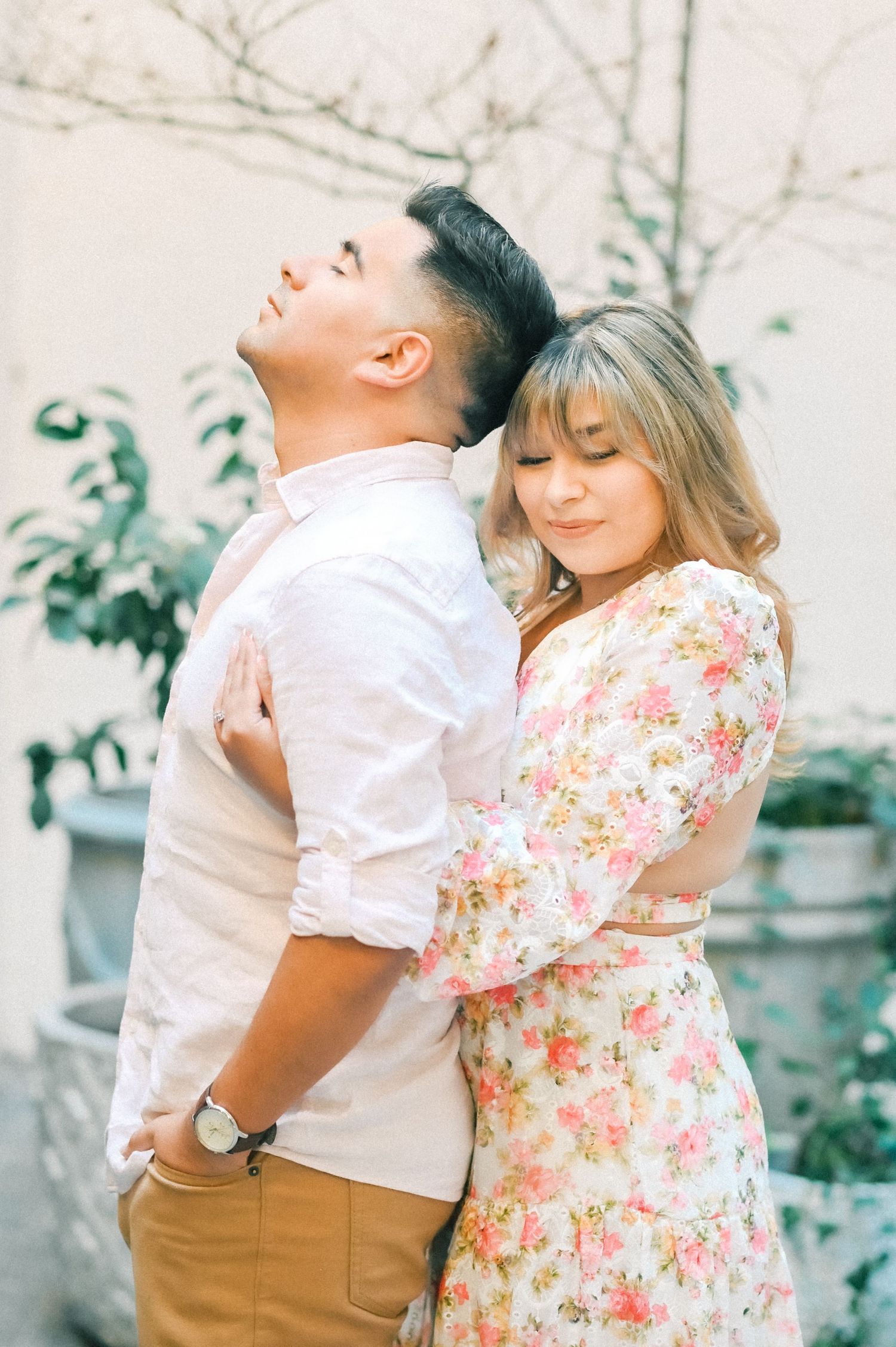 Couple embracing tenderly outdoors, woman in floral dress hugging man in white shirt.