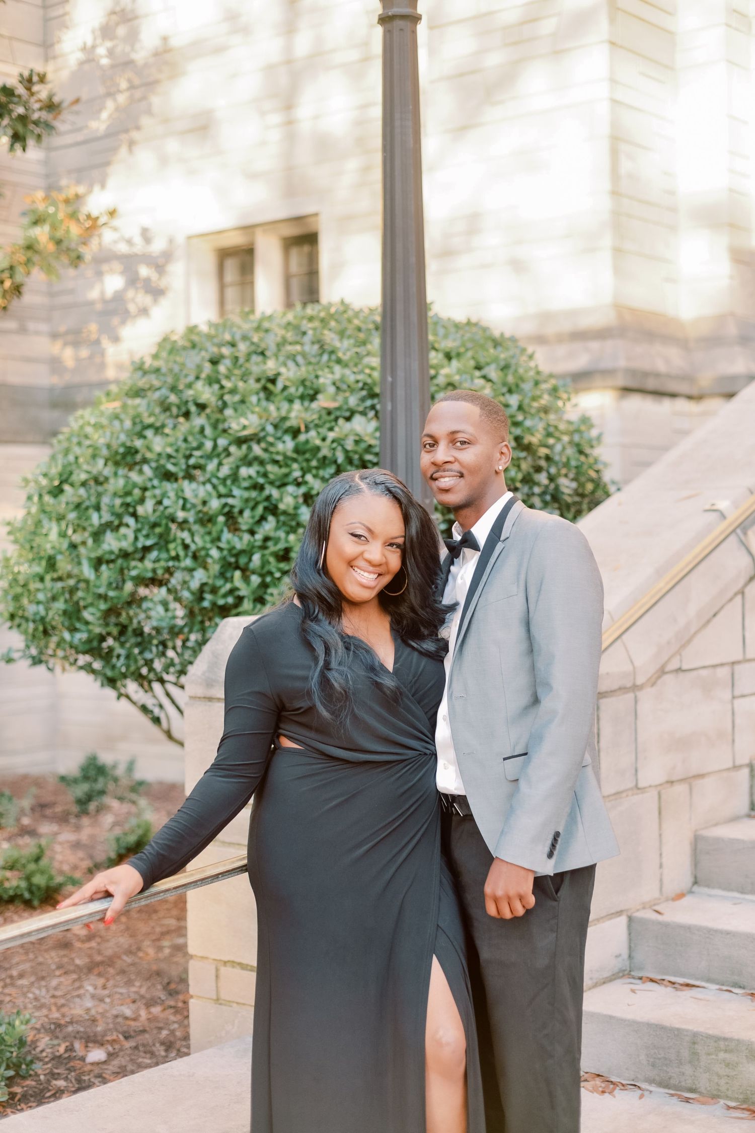 Smiling couple in elegant black and grey formal wear posing on outdoor stone steps.