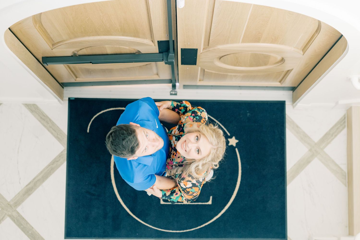 Aerial view of couple standing together on a navy blue rug beneath an ornate ceiling.