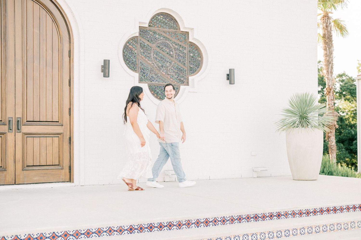 People walking down a white-walled Mediterranean style corridor with arched doorways and tiled accents.