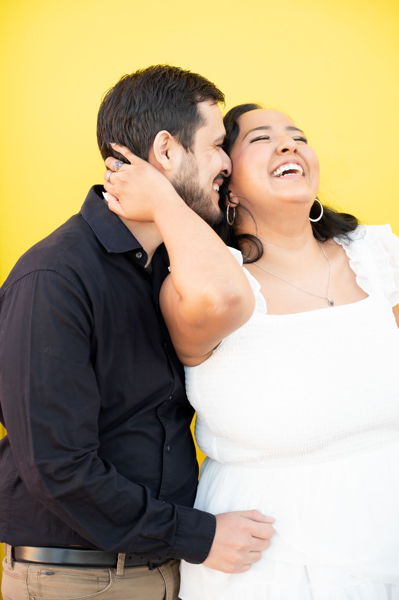 A couple shares an intimate embrace against a vibrant yellow background, capturing a joyful candid moment.