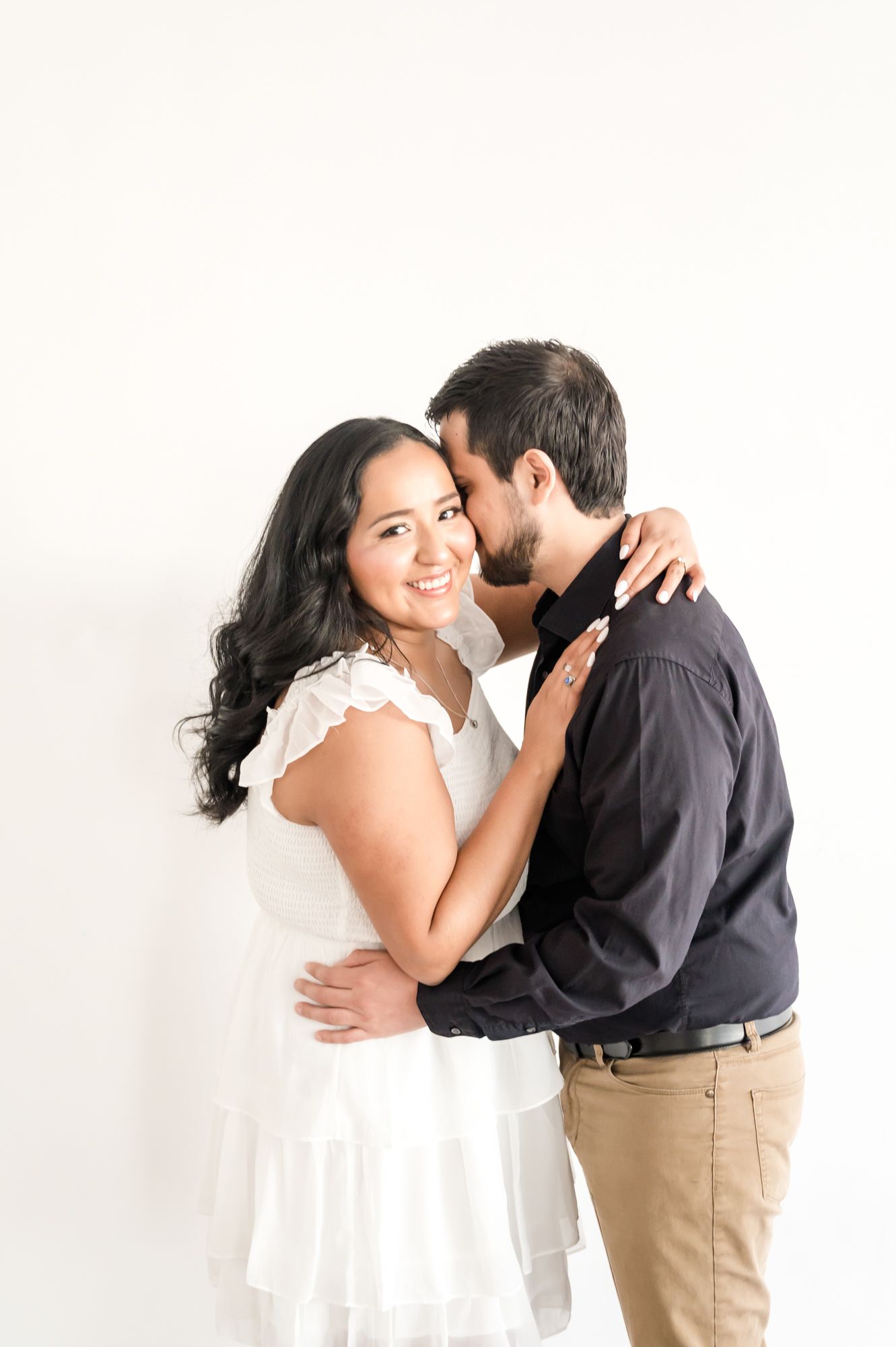 Joyful couple embracing and laughing during engagement photo session against white backdrop.