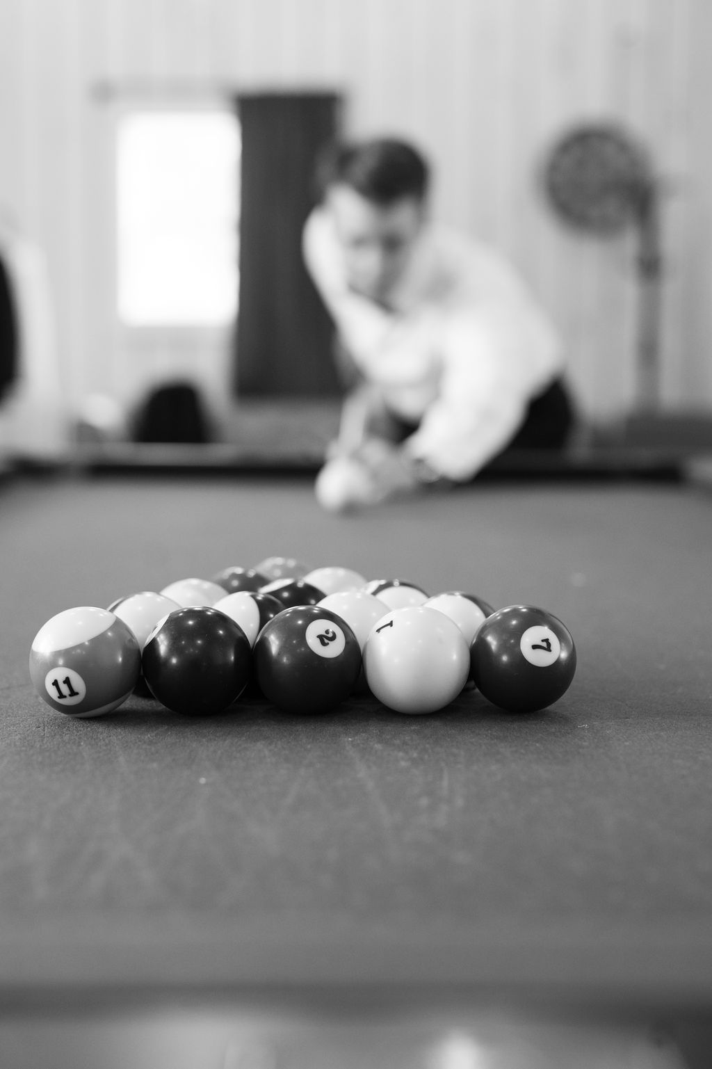 Black and white photo of a man preparing to break billiard balls racked on a pool table.