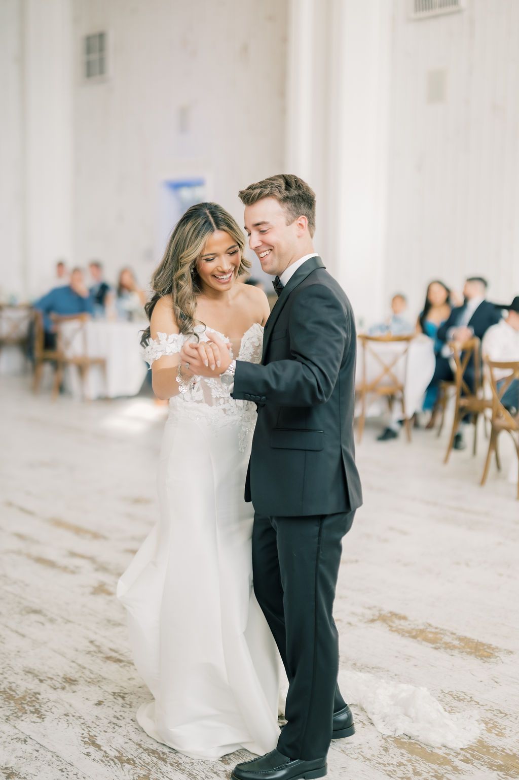Bride and groom share a joyful first dance at their elegant wedding reception, smiling and holding hands.