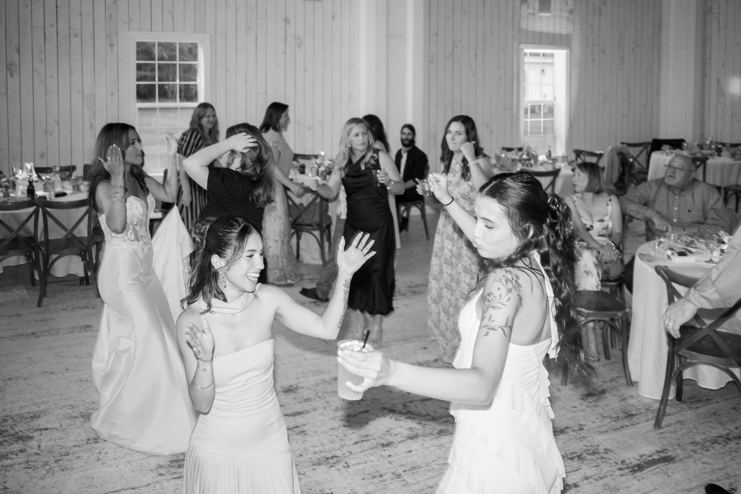Bridesmaids and guests dance joyfully on the dance floor during a wedding reception in black and white photo.