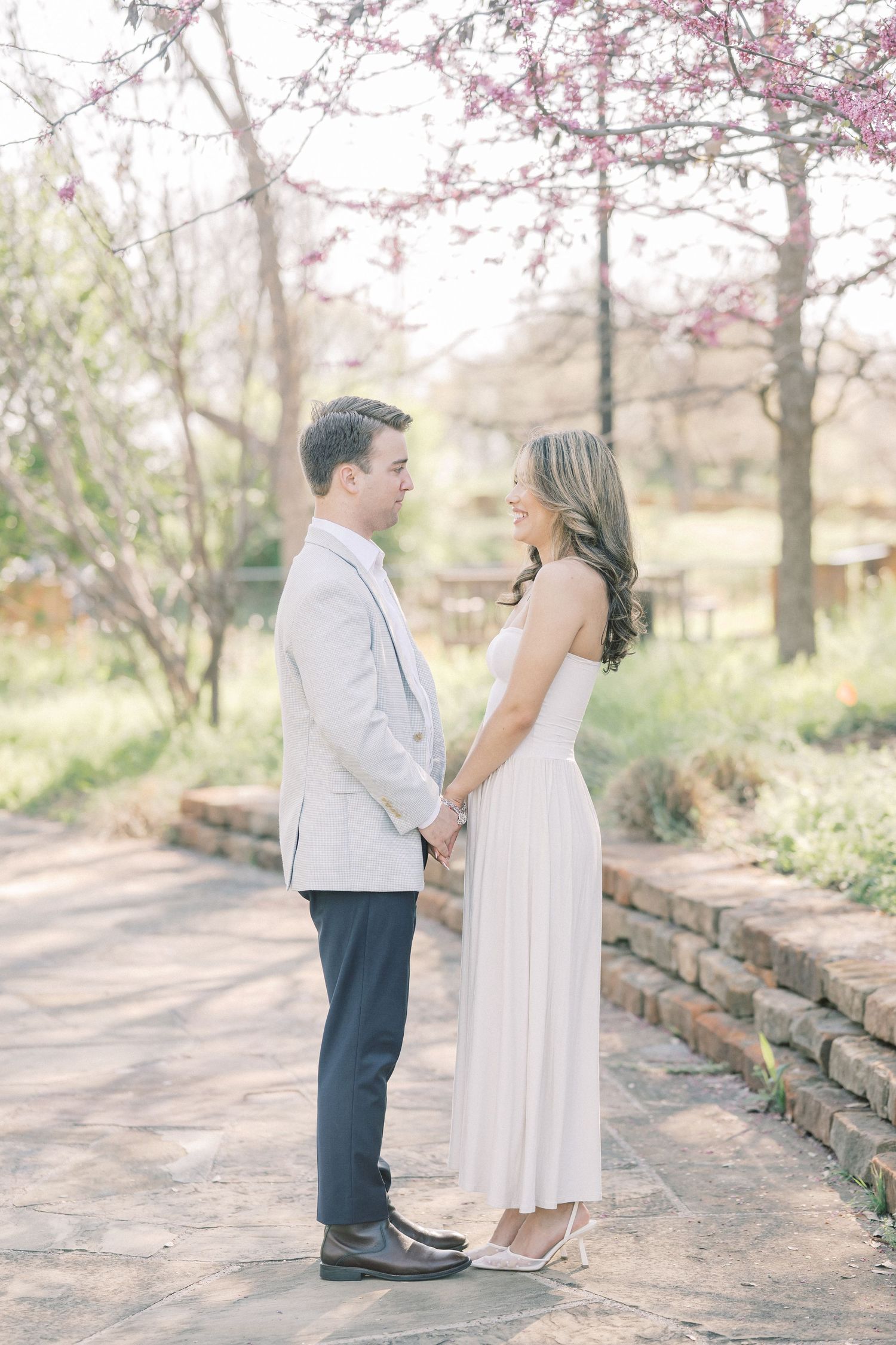 A romantic springtime engagement photo with cherry blossoms blooming above a couple on a stone path.