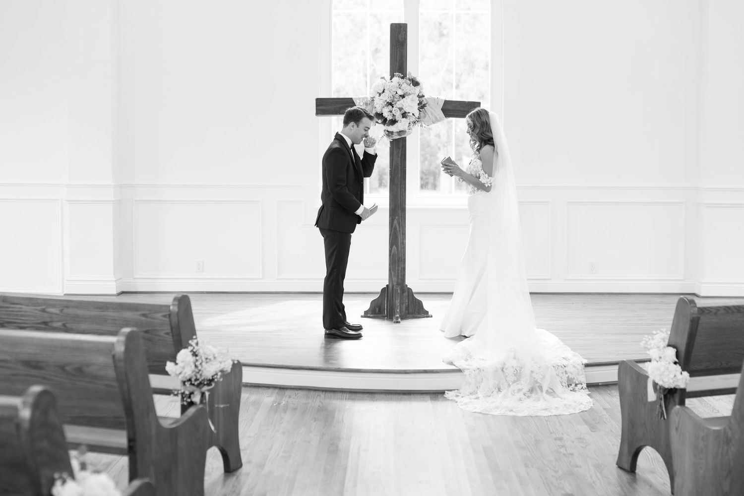 Black and white photo of bride and groom exchanging vows at church altar with wooden cross.