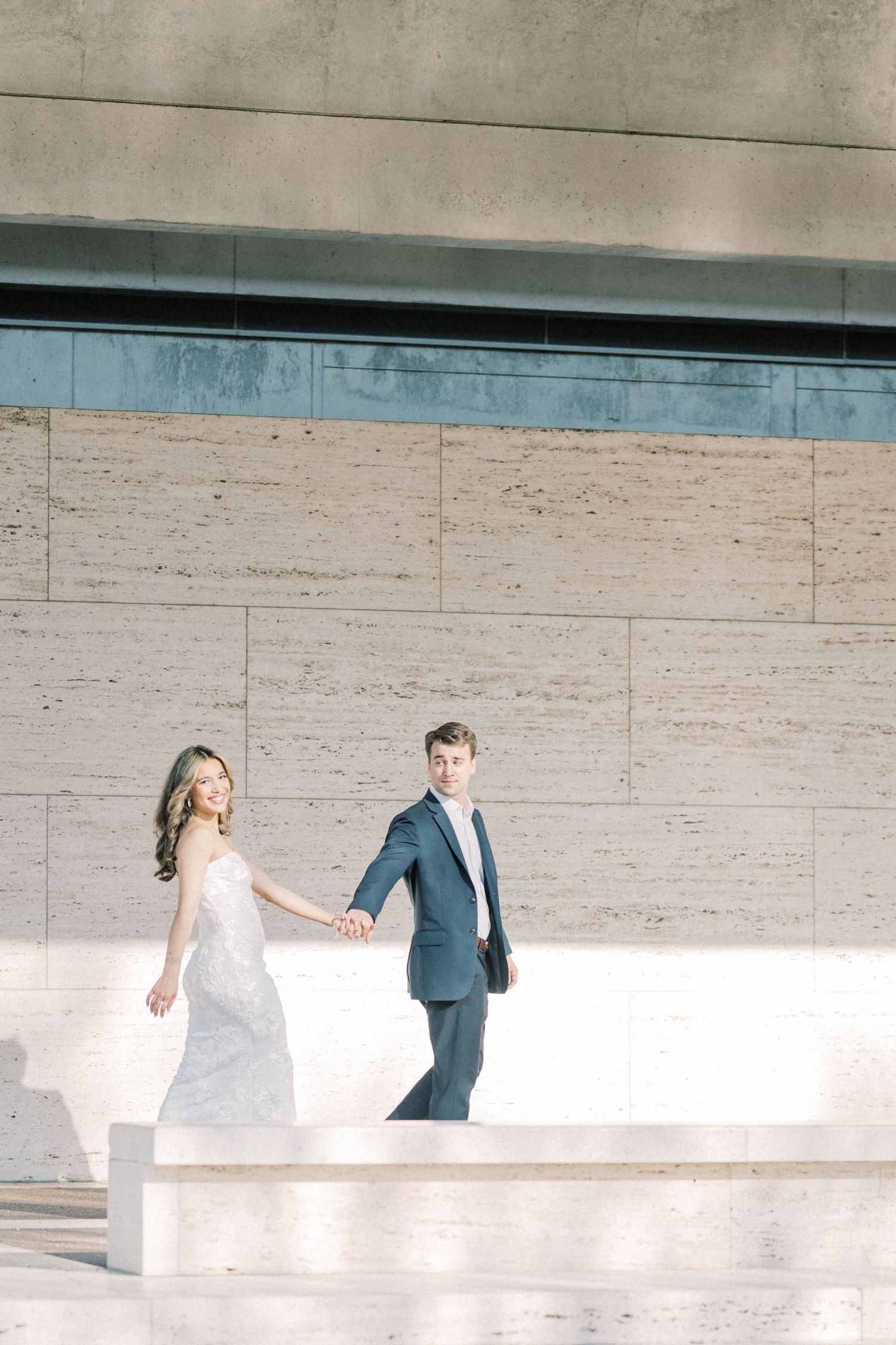 A minimalist wedding sequence shows a couple walking through a bright white modern architectural space with stone walls.