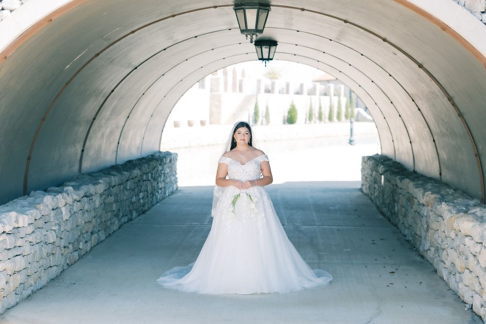 A bride in a white wedding gown poses in a stone tunnel with natural lighting creating a romantic atmosphere.