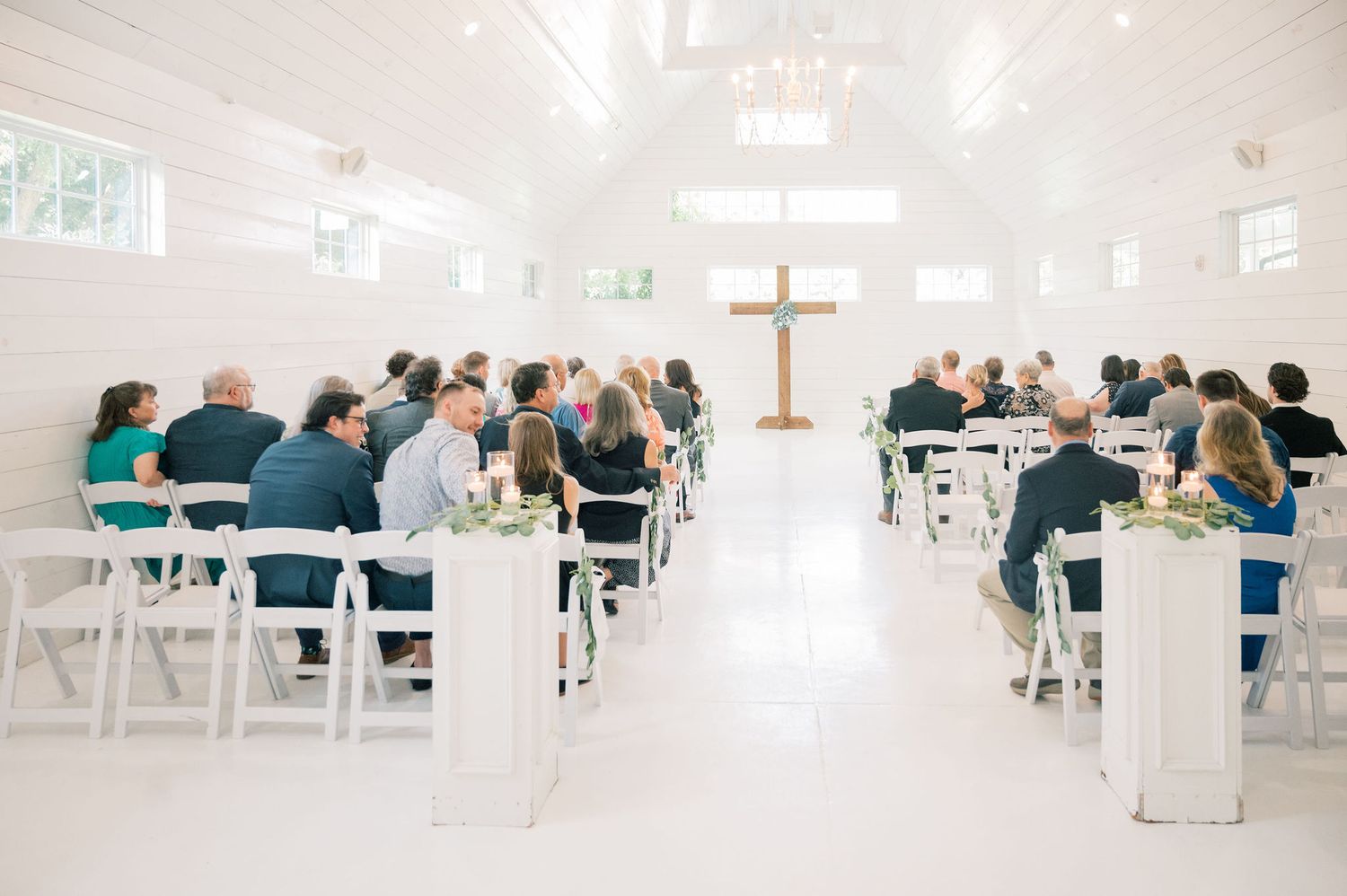 A bright white church interior with rows of chairs and guests seated for a wedding ceremony.