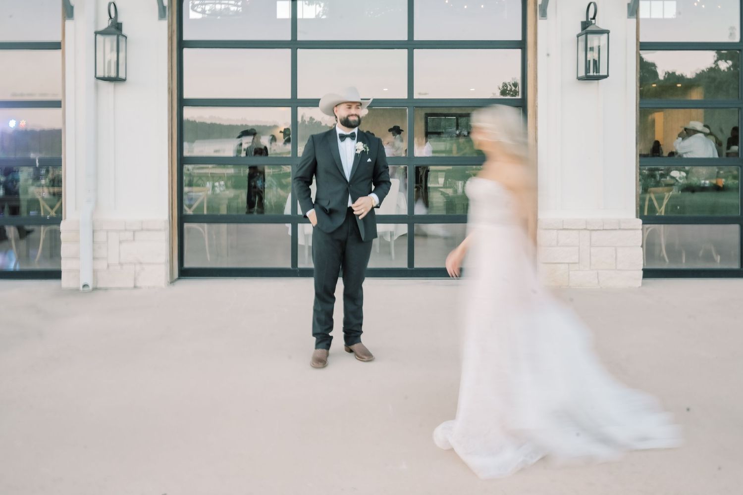 Groom in dark suit watches bride approach in flowing white gown during outdoor first look.