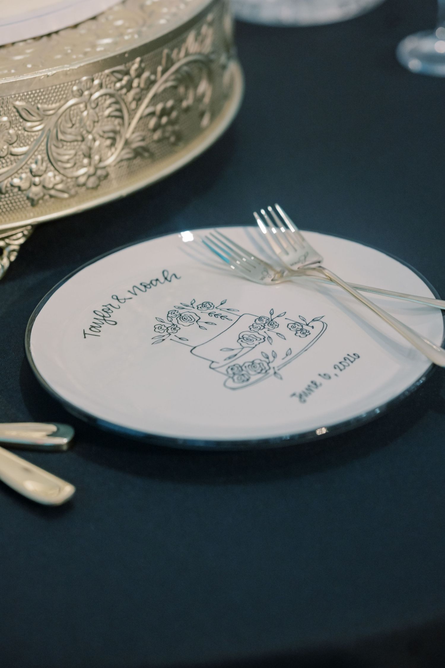 Custom wedding plate with illustrated monogram and date June 3 2023 with silver forks on a dark tablescape.