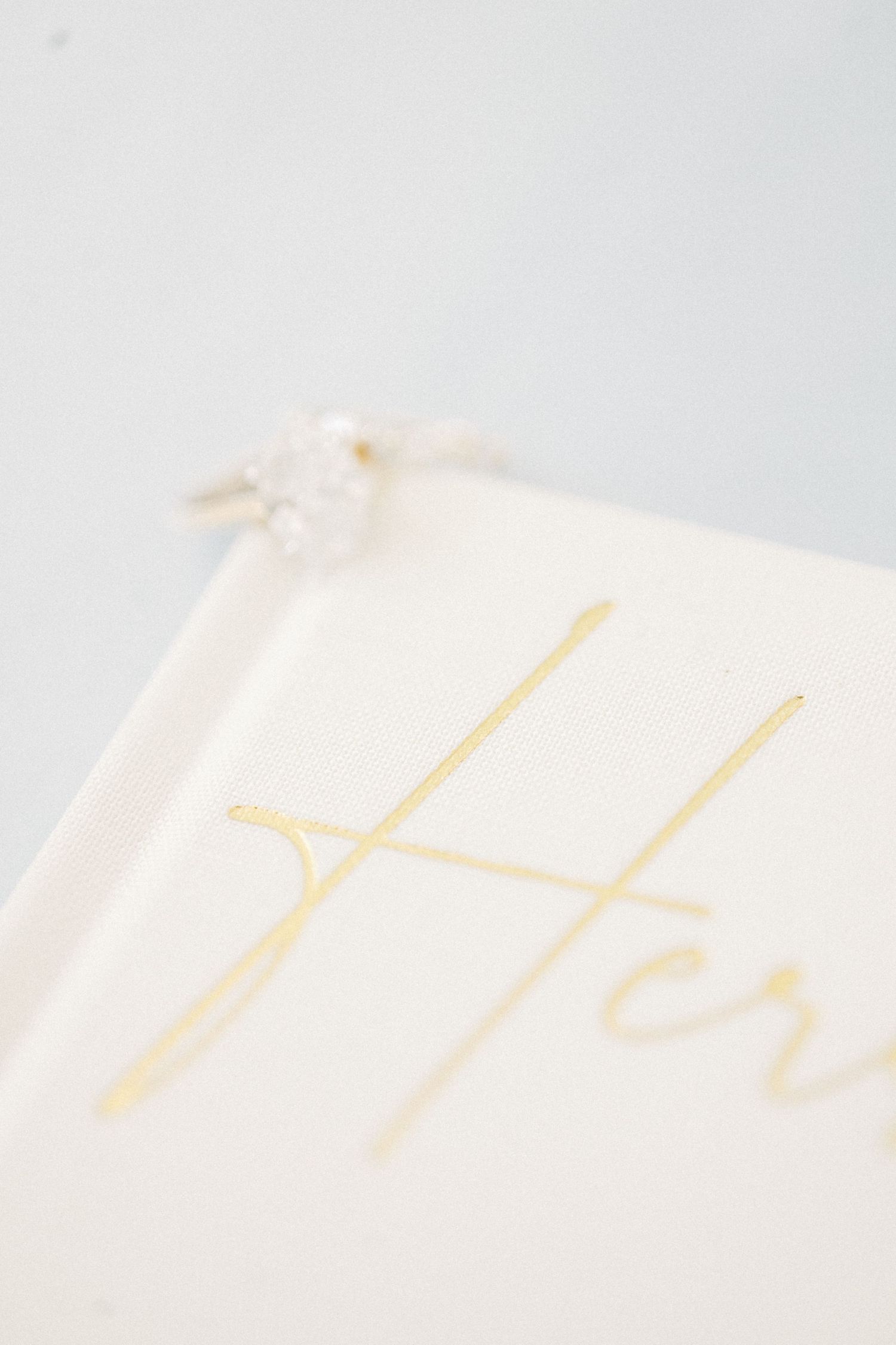 Close-up of a white wedding vow book with gold foil script lettering and a diamond ring resting on top.