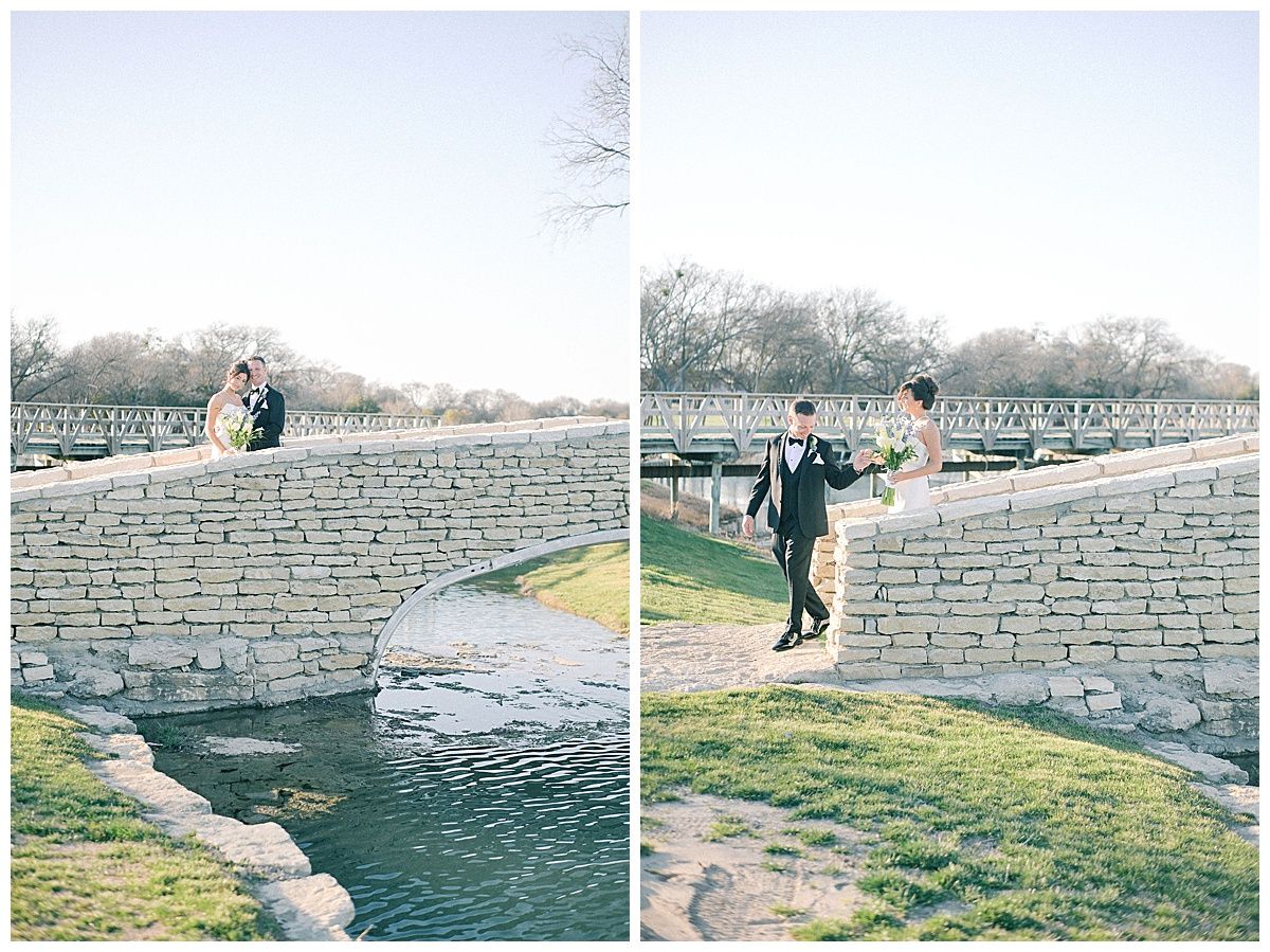 Wedding couple poses along stone retaining wall near water feature.