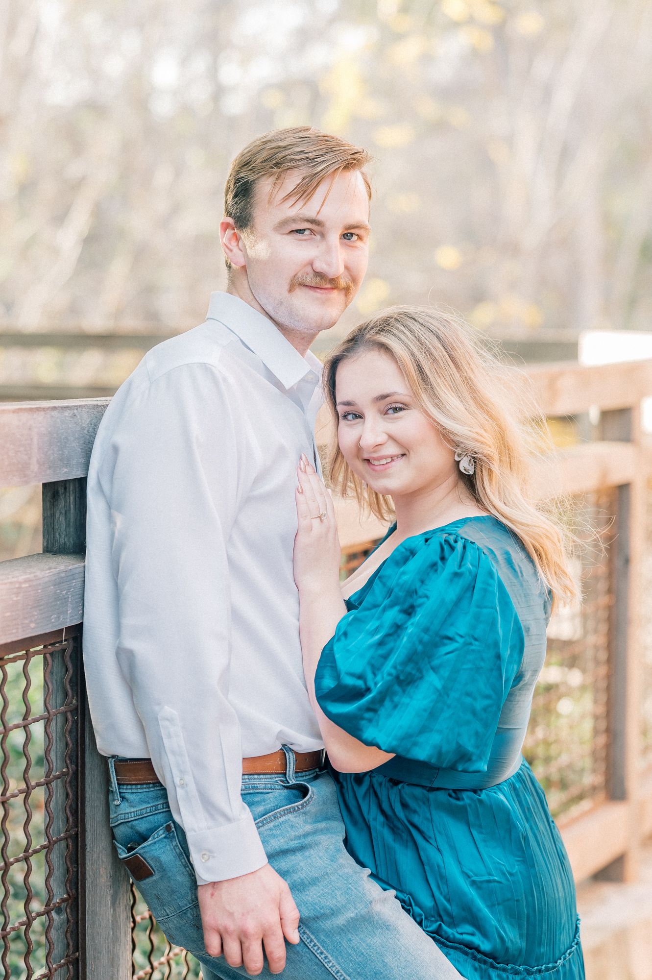 A romantic couple shares a tender moment on a wooden deck, with her wearing a vibrant teal blouse.