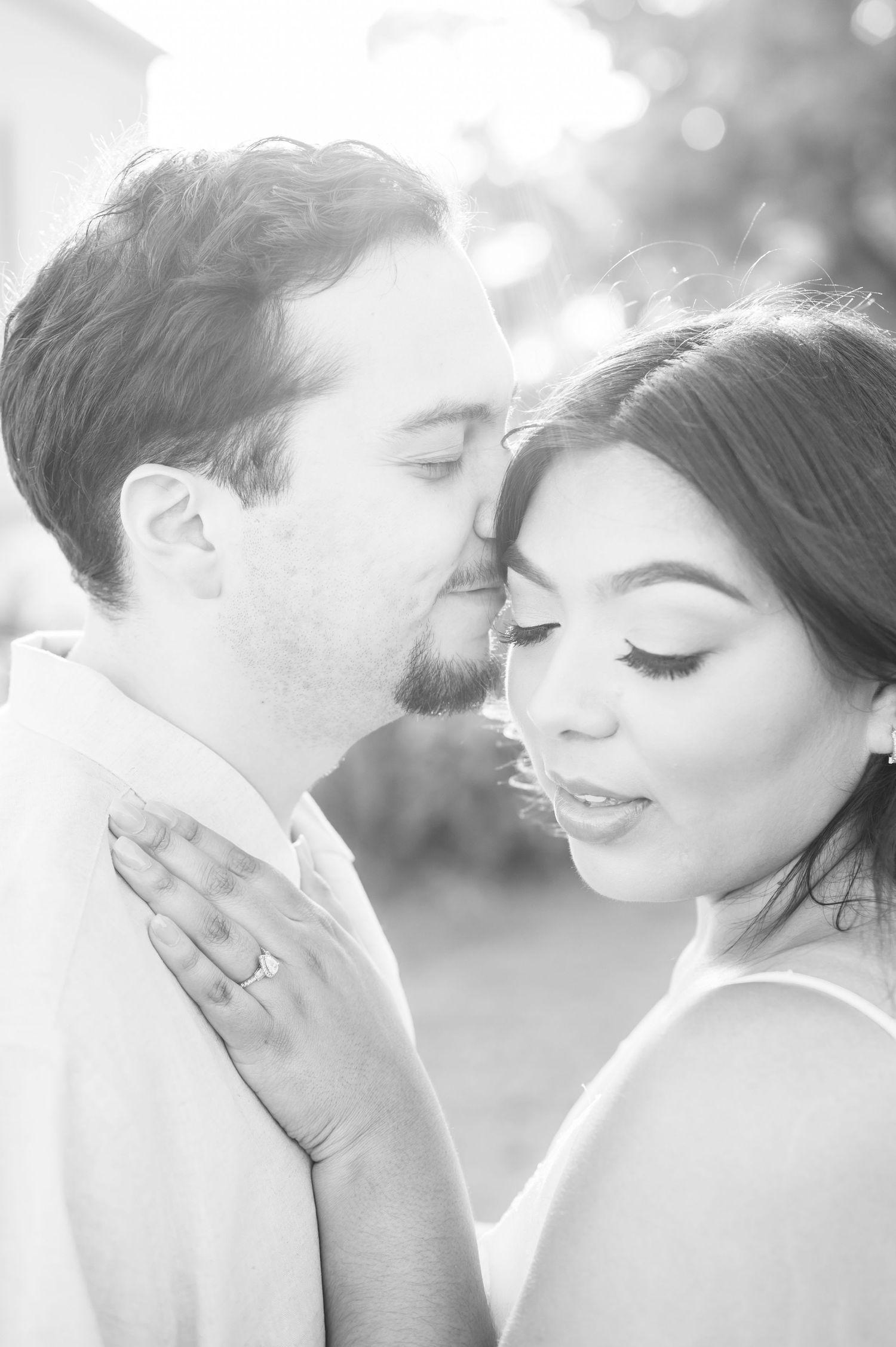 Black and white portrait of newlyweds sharing tender moment outdoors with dreamy lighting effect.