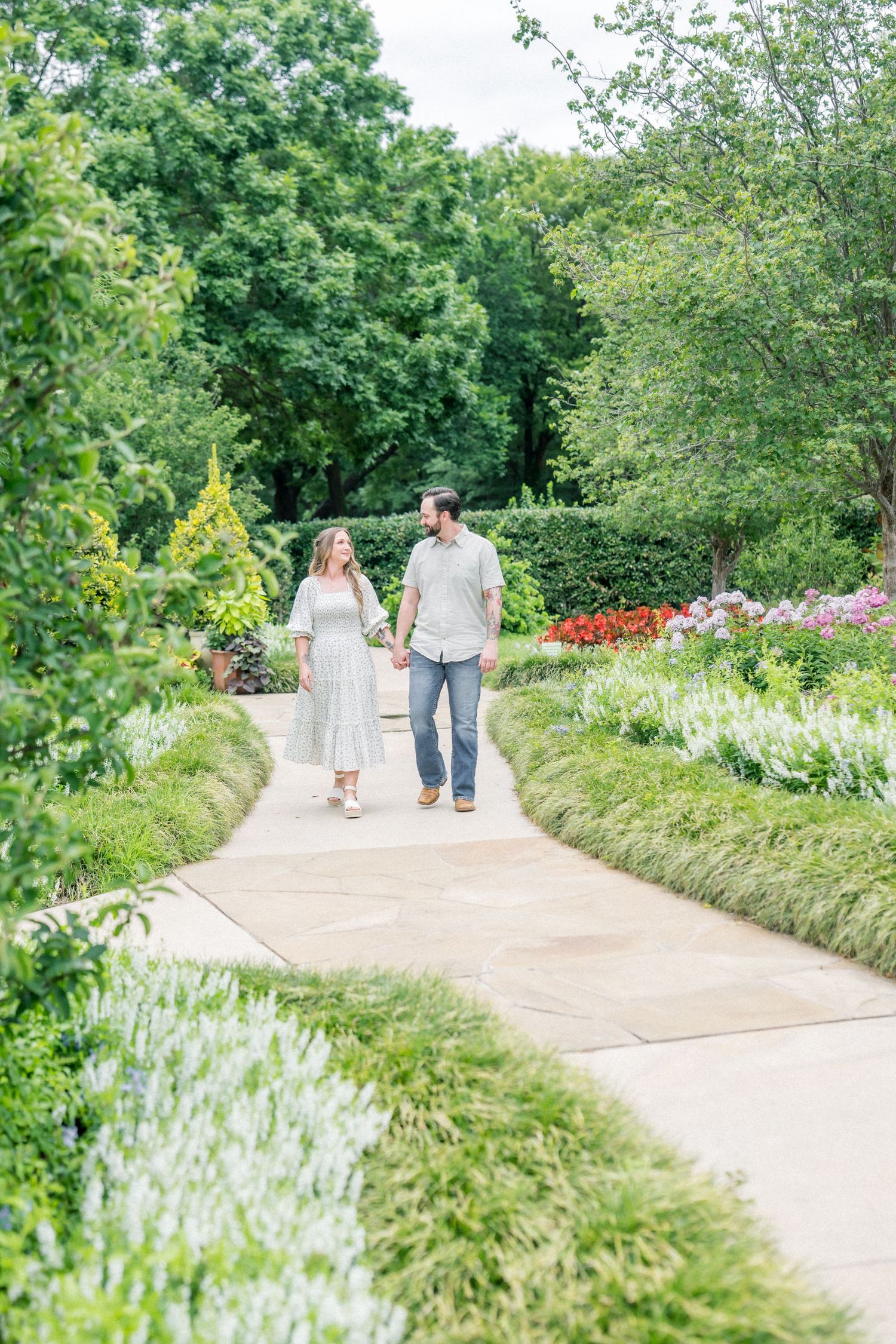 Couple walking hand in hand along a scenic garden pathway with colorful blooms.