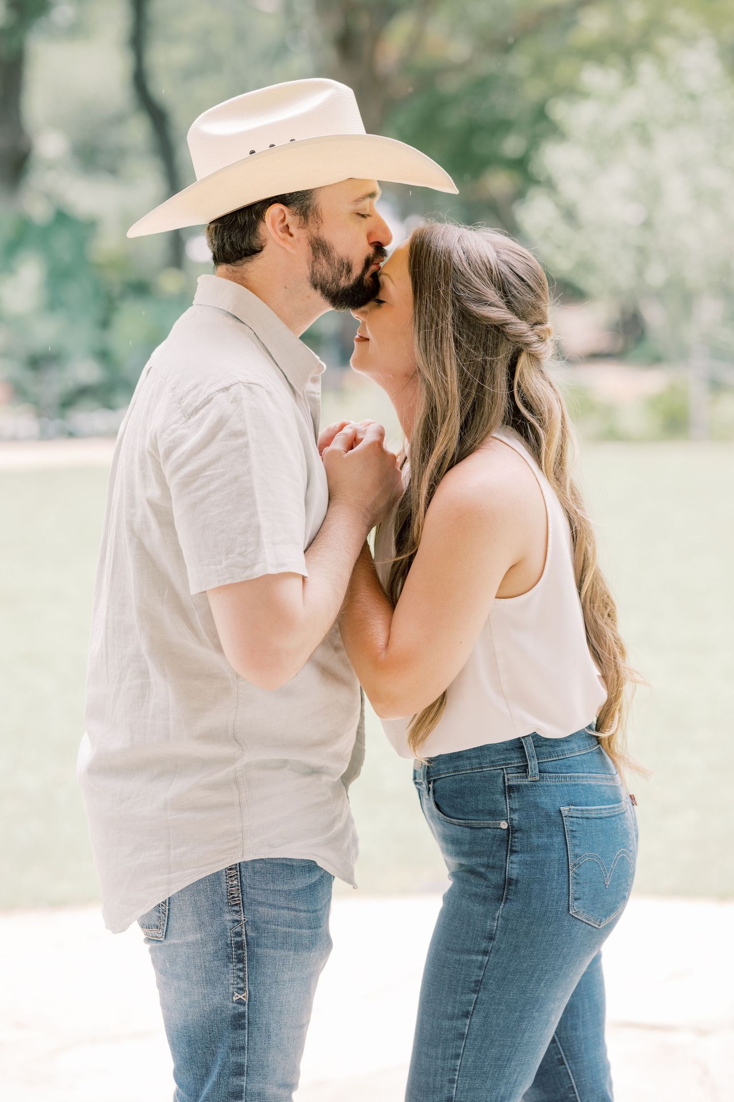 Couple sharing a kiss outdoors, man wearing a cowboy hat.