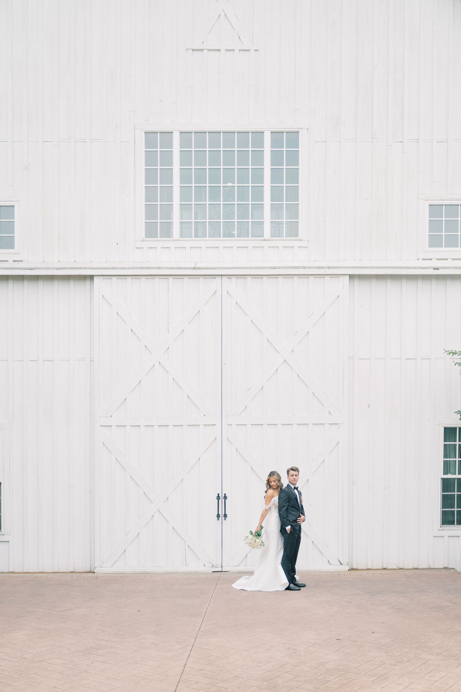Bride and groom posing together in front of large white barn doors at wedding venue.