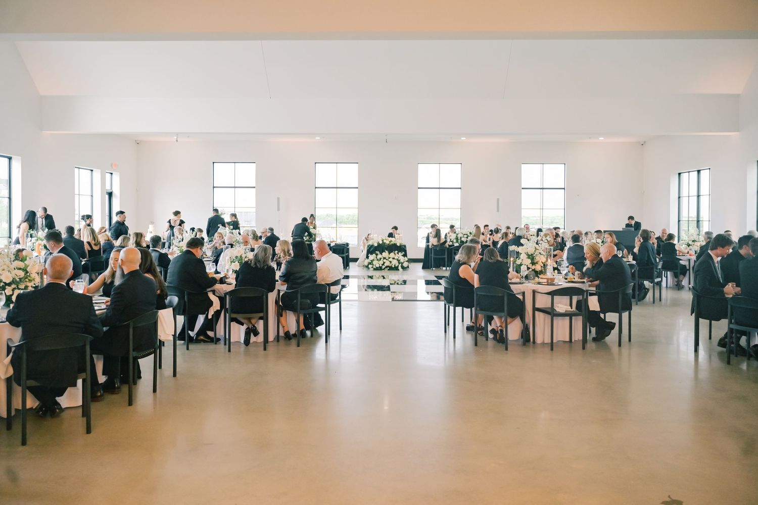 Elegant wedding reception hall filled with guests seated at tables with floral centerpieces.