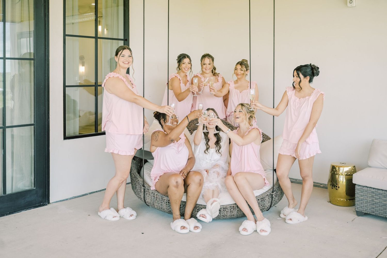 Bridesmaids in pink pajamas and slippers celebrate with bride during wedding morning getting ready party.
