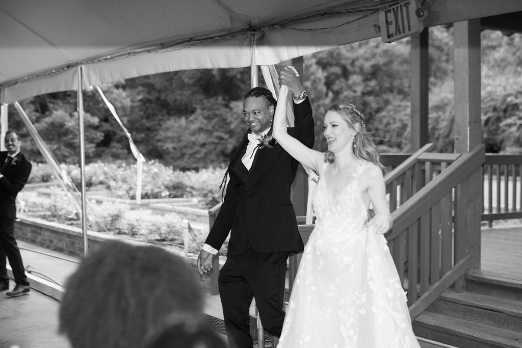 Black and white photo of a bride and groom raising hands in celebration at their wedding reception entrance.