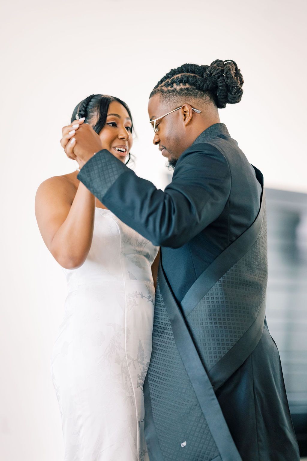 A groom in a dark suit adjusts his bride's hair as she smiles in a white wedding dress.