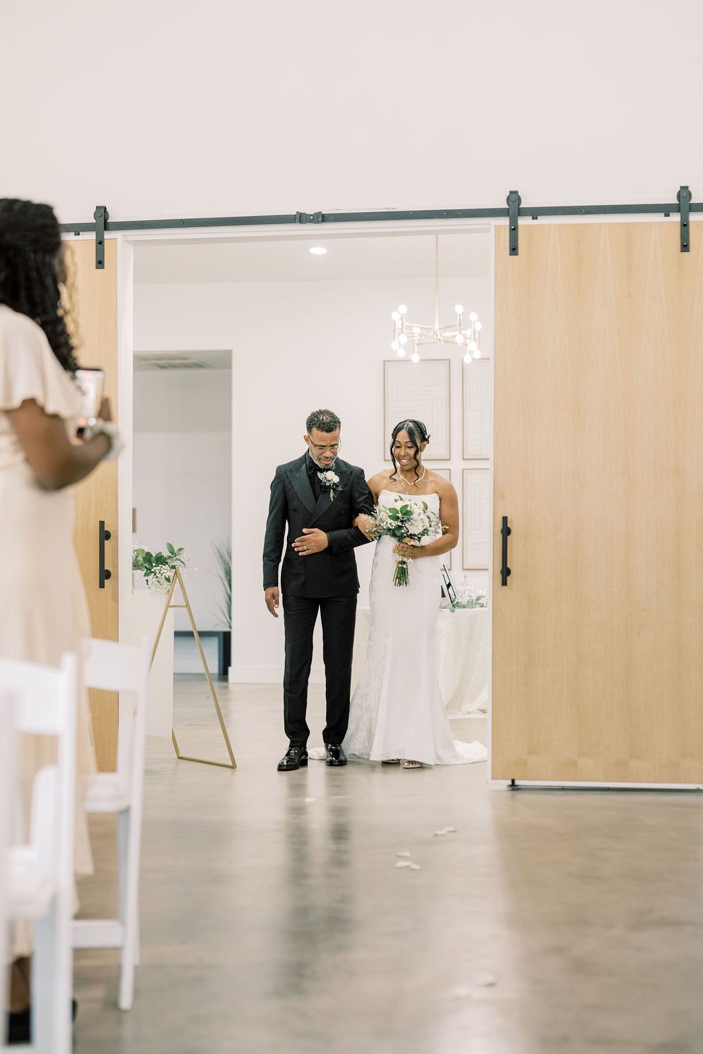 Bride and groom entering wedding ceremony through wooden barn doors in elegant white venue.