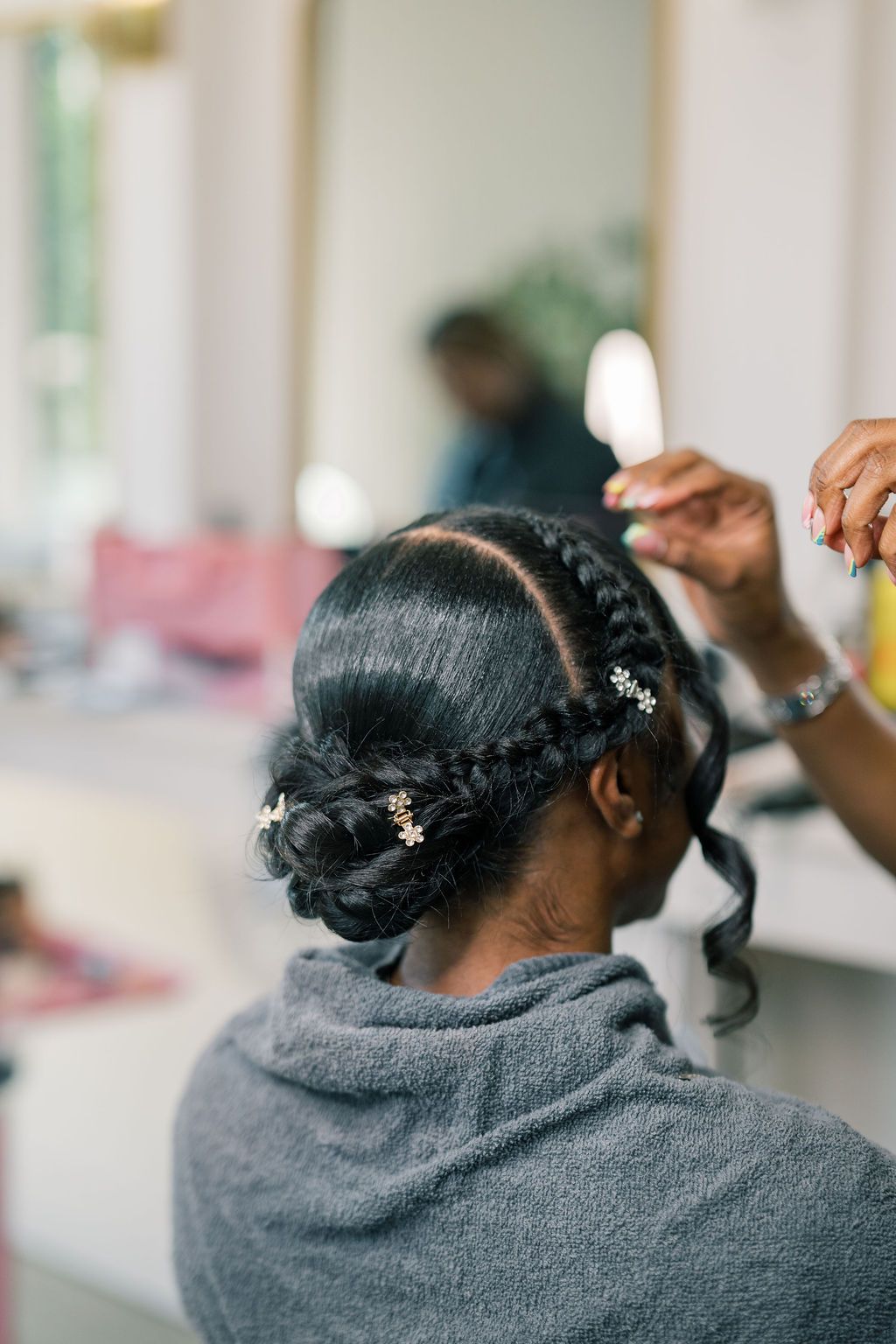 Hairstylist adding floral pins to elegant braided updo on Black bride during wedding preparation.