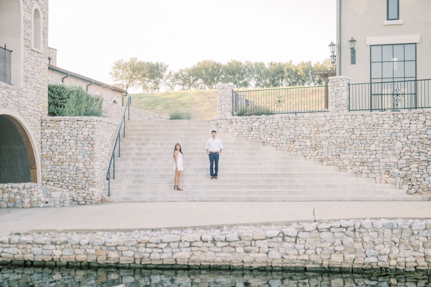 Couple standing on stone steps near a water feature at an elegant outdoor venue during golden hour.