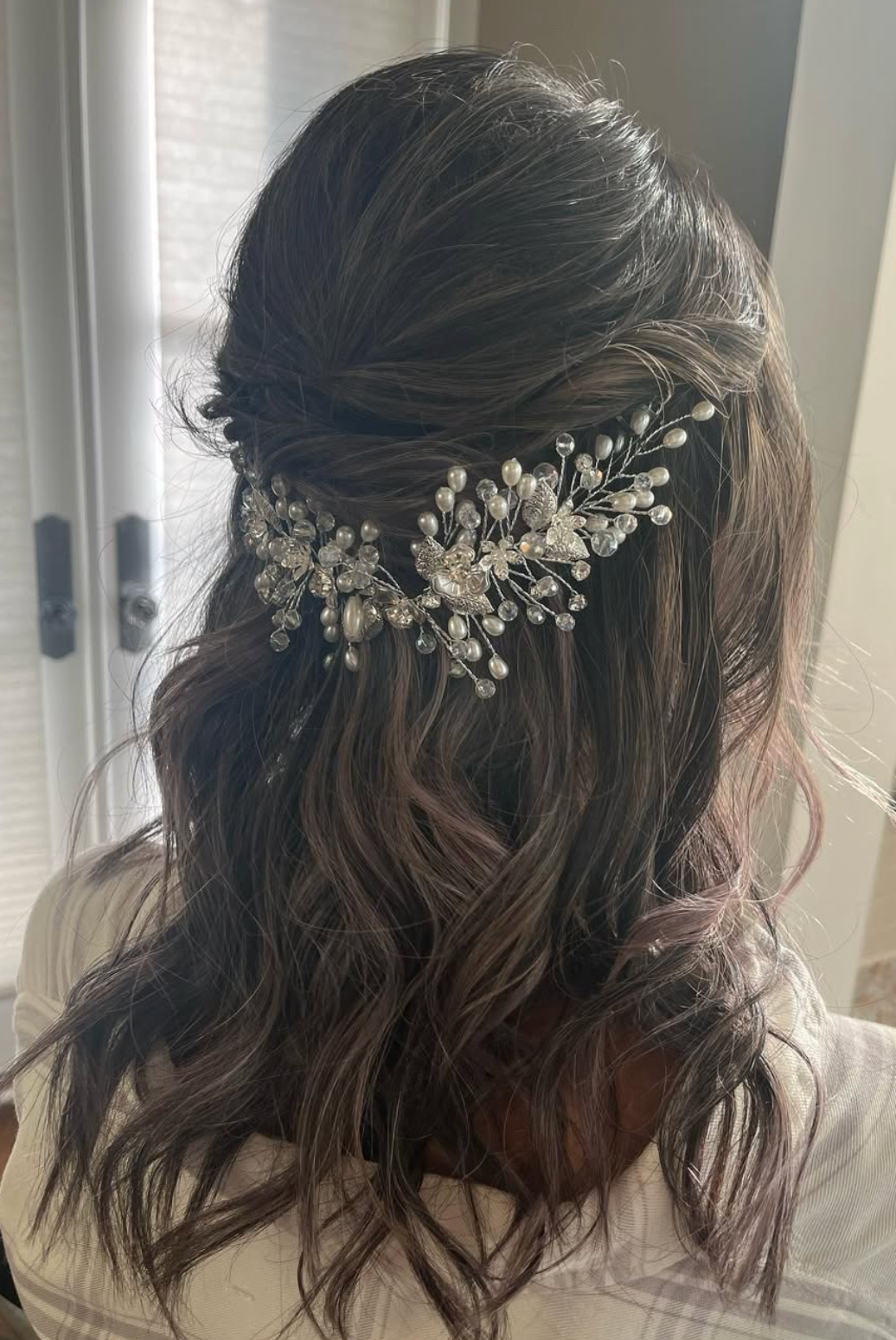 Elegant half-up bridal hairstyle with pearl and crystal hair comb accessory on dark wavy hair.