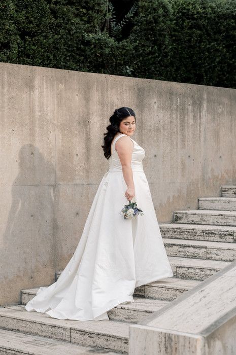 Bride in white ball gown with train descends stone steps holding a bouquet outdoors.