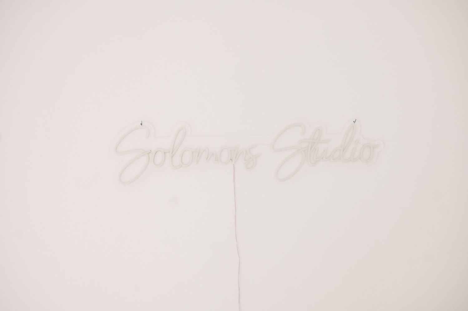 Solomons Studio neon sign mounted on a white wall, glowing softly in cursive lettering.