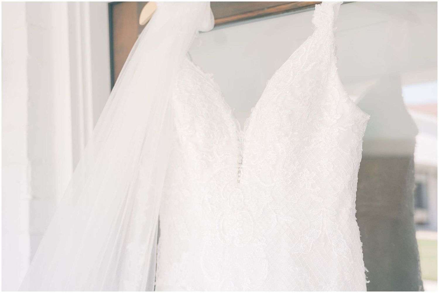 White wedding dress hanging elegantly against a light background, showcasing delicate lace details and flowing fabric.