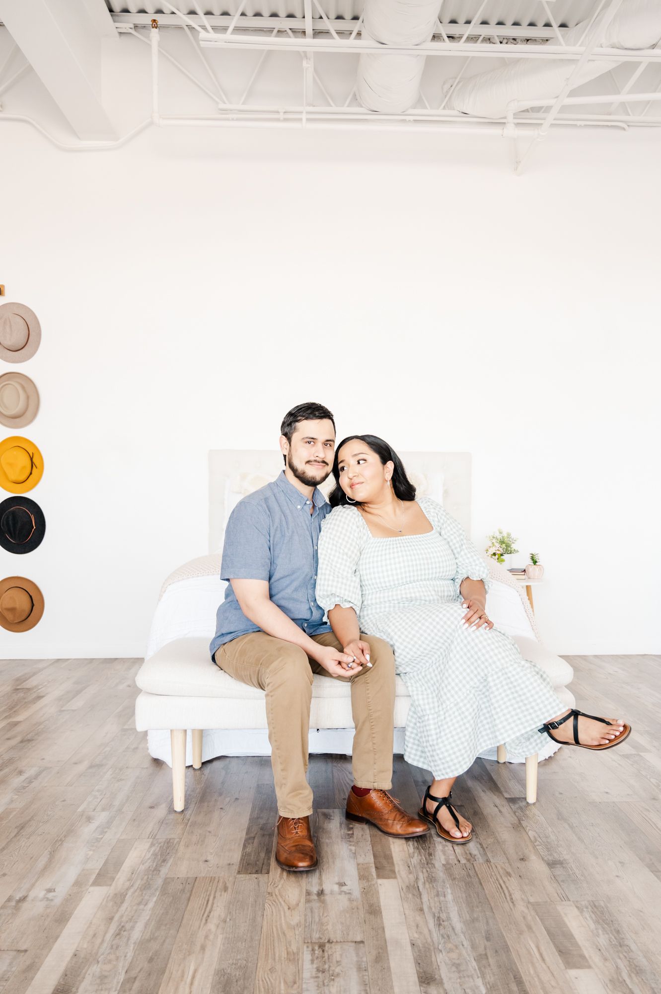 A couple sits together on a white bench in a minimalist studio setting.